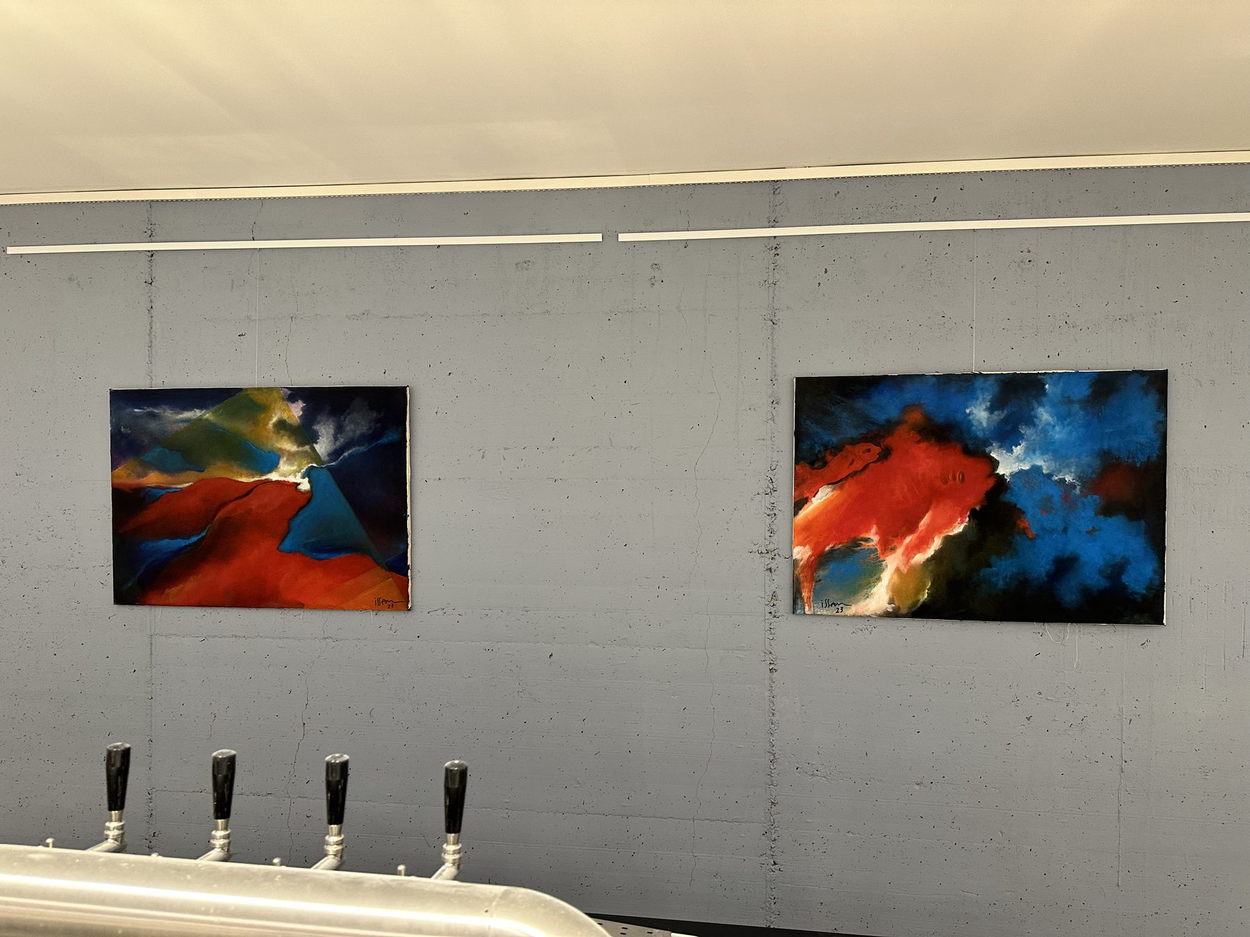 Zwei abstrakte Gemälde an einer Betonwand über einer Bar